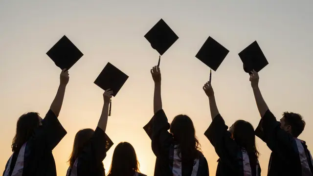 Silhouetted graduates hold their graduation caps aloft against a warm golden sunset sky