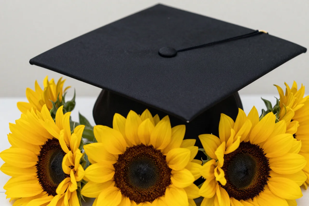 A black graduation cap with a gold tassel accent rests atop a cluster of bright yellow sunflowers.