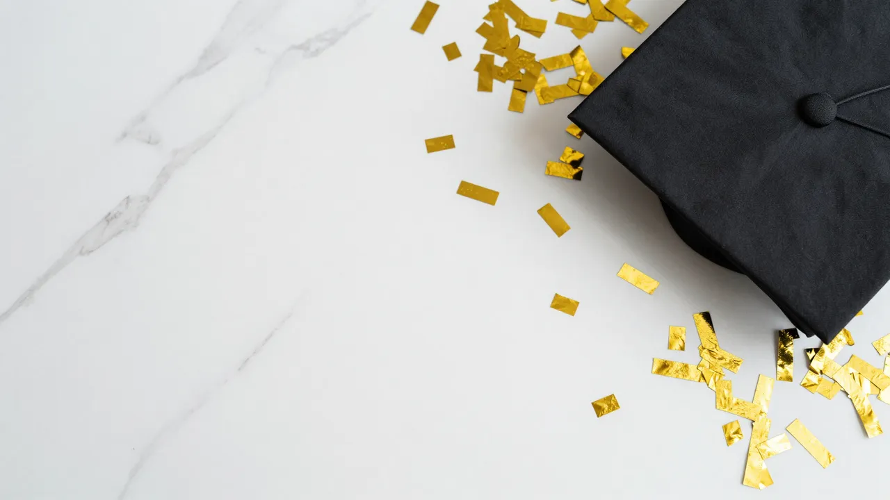 Black graduation cap and scattered gold confetti rest on the right of a white marble surface with empty copy space on the