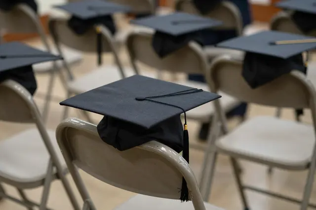 Black graduation caps rest on rows of light folding chairs ahead of a graduation ceremony