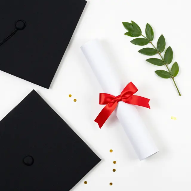 Top down flat lay of graduation caps, diploma scroll, laurel sprig, and gold confetti on a plain white background