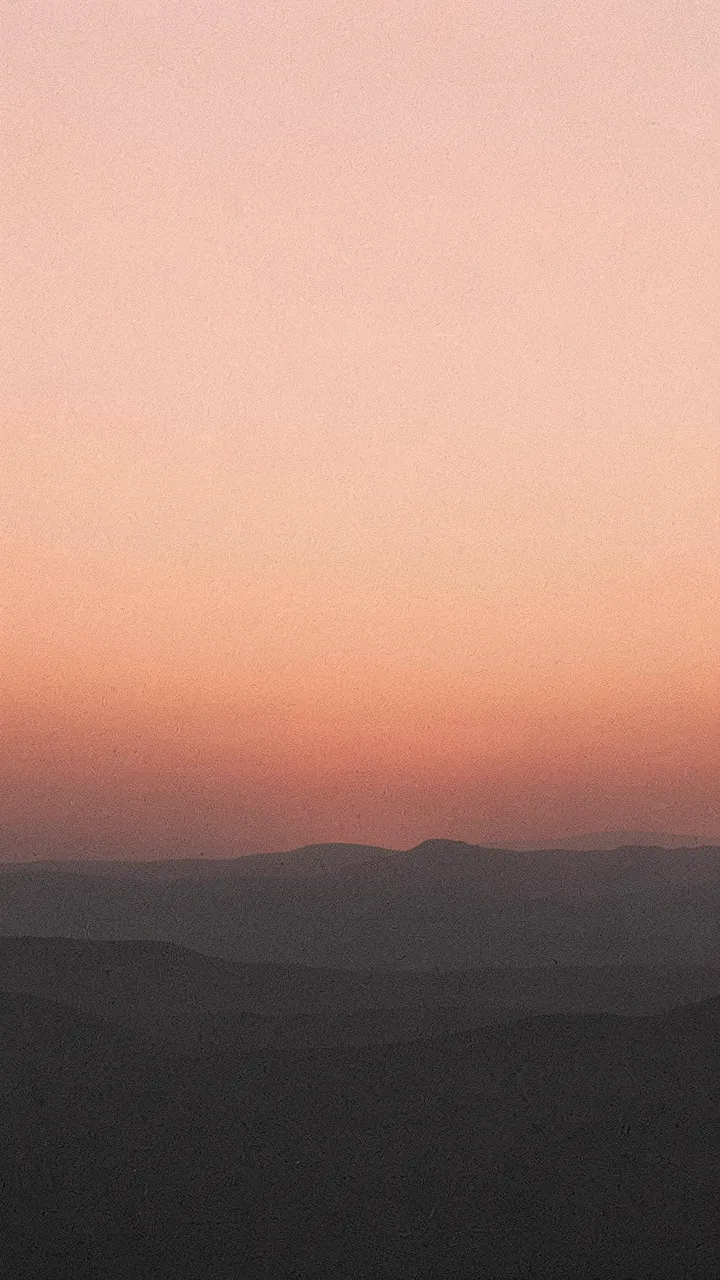Vertical grainy gradient of peach sunrise sky above dark charcoal mountain silhouettes