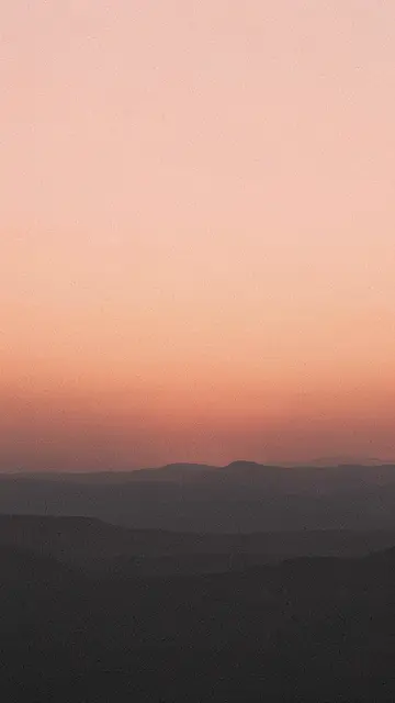 Vertical grainy gradient of peach sunrise sky above dark charcoal mountain silhouettes