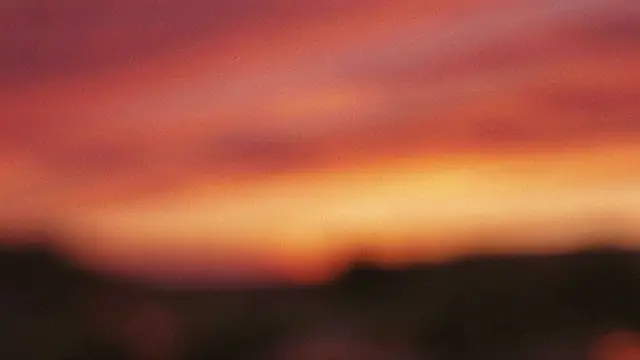 Blurred grainy sunset gradient shifting from deep crimson to warm amber above dark silhouetted land