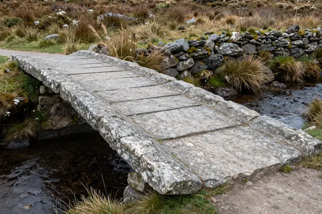 A flat stone clapper bridge crosses a small moorland stream beside a dry stone wall