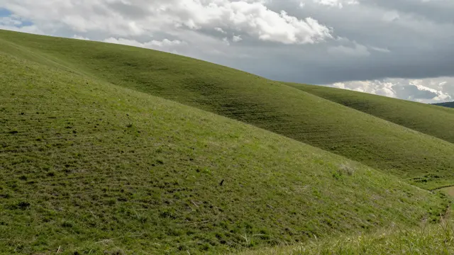 Smooth green rolling grass hills stretch beneath a sky of drifting clouds and soft cloud shadows.