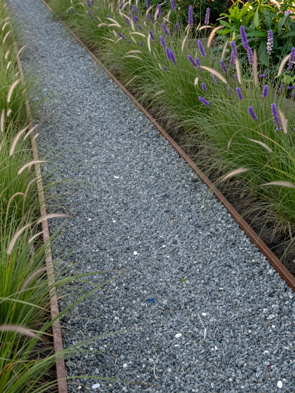 A pea gravel walkway edged with steel runs through ornamental grasses and purple flowering plants.