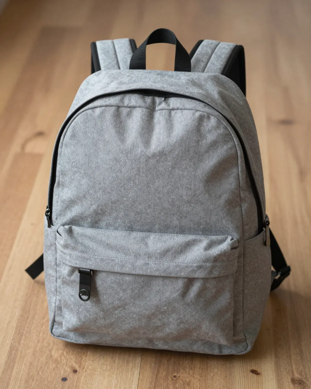 Front view of a plain gray canvas backpack standing upright on a light wooden floor.