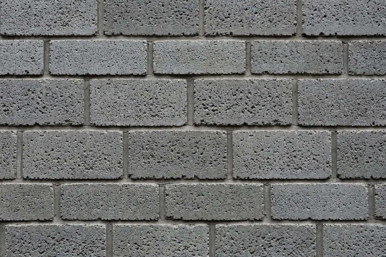 Full frame close-up of a rough pitted gray cinder block wall laid in staggered courses