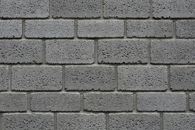 Full frame close-up of a rough pitted gray cinder block wall laid in staggered courses