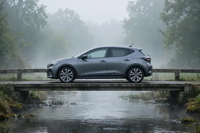 A gray modern hatchback sits on a concrete bridge spanning a river in thick morning fog.