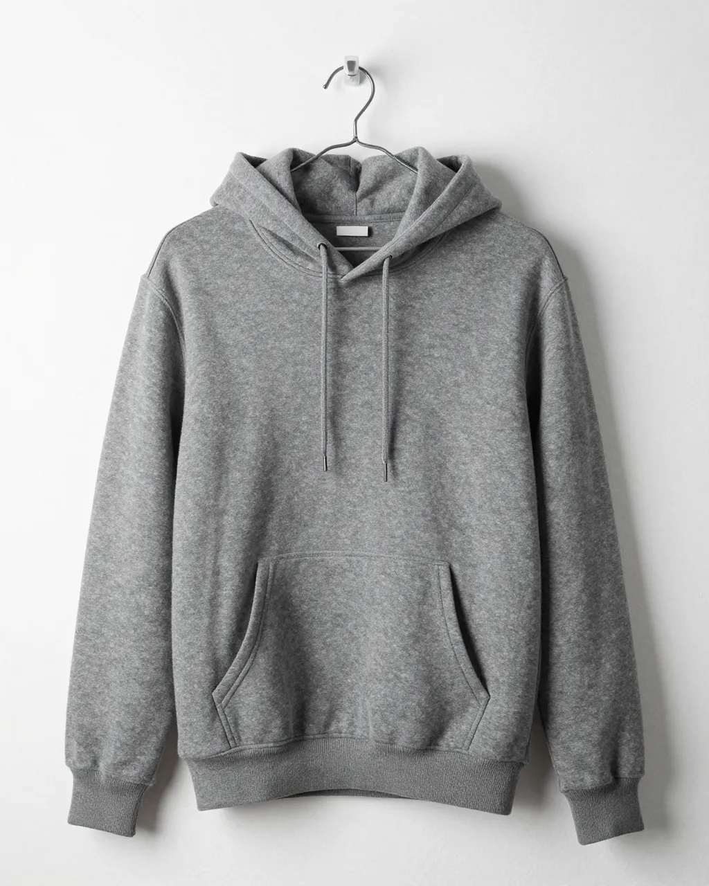 Plain charcoal gray hoodie hangs from a wall hook against a smooth white plaster wall