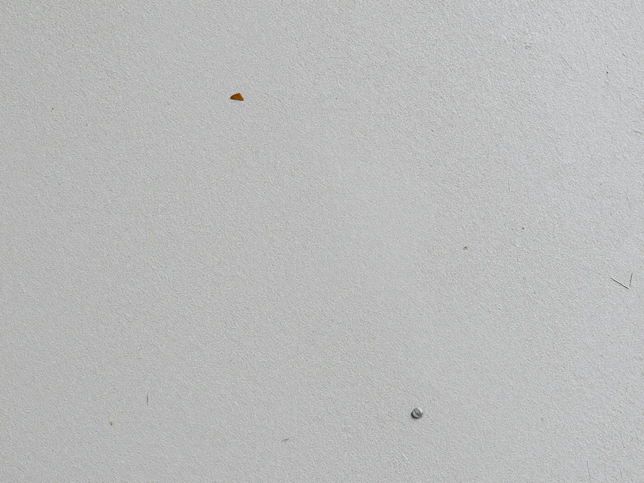 Full frame close-up of a matte light gray pressed chipboard surface with scattered tiny flecks