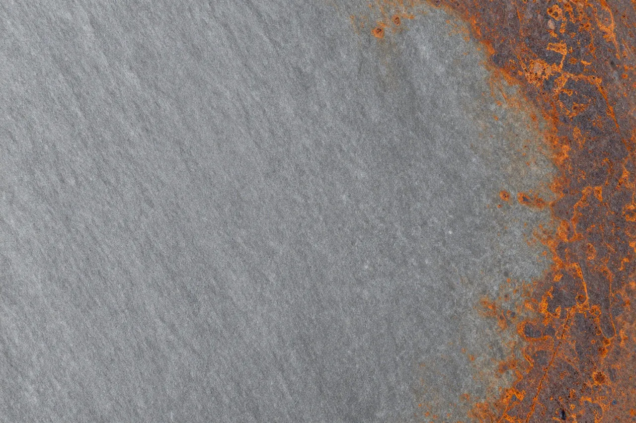 Full frame close-up of gray slate surface with patchy orange-brown rust-colored stains along one edge