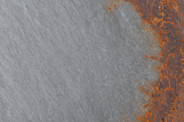 Full frame close-up of gray slate surface with patchy orange-brown rust-colored stains along one edge