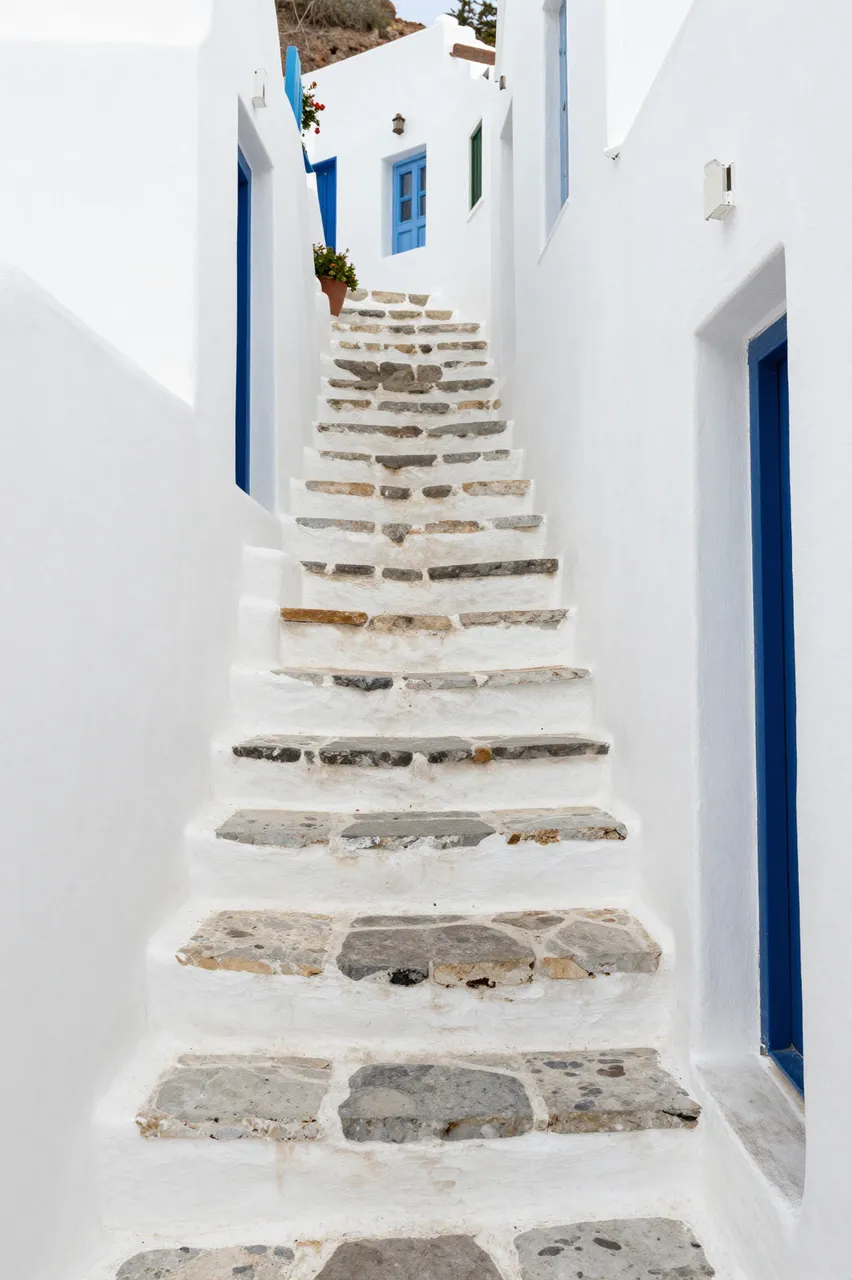 Winding stone steps lead up between whitewashed Greek village buildings with bright blue doors