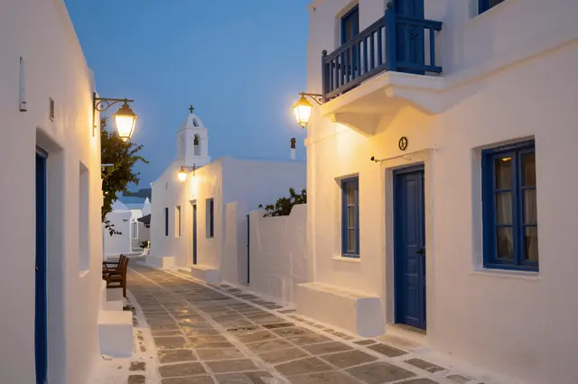 Whitewashed Cycladic village street with glowing wall lamps during blue hour twilight in Greece