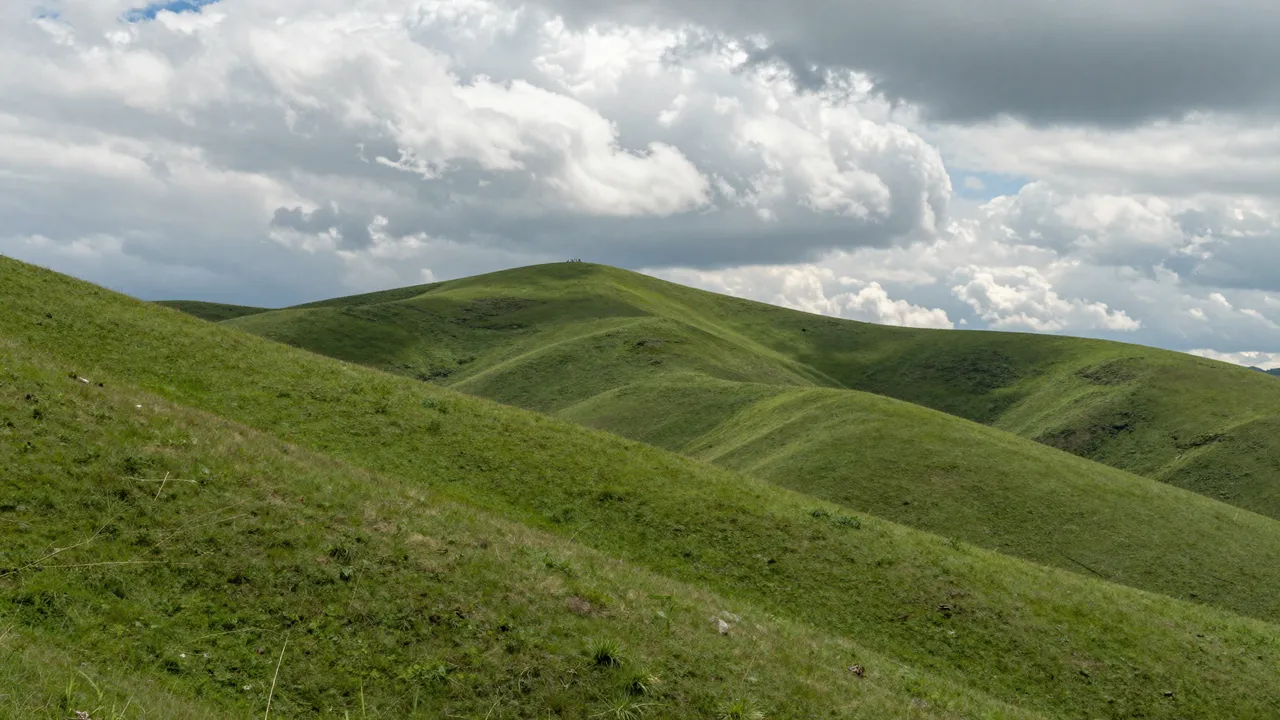 Rolling lush green hills stretch below tall, billowing summer cumulus clouds.
