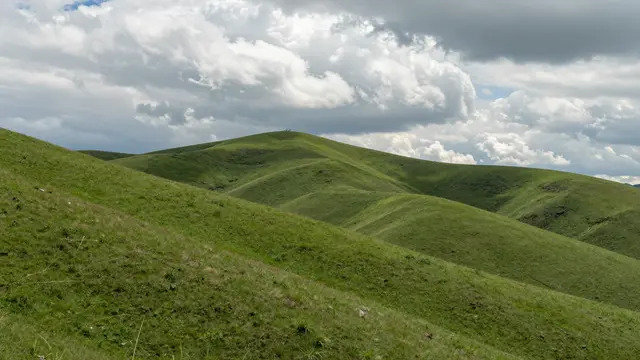Rolling lush green hills stretch below tall, billowing summer cumulus clouds.