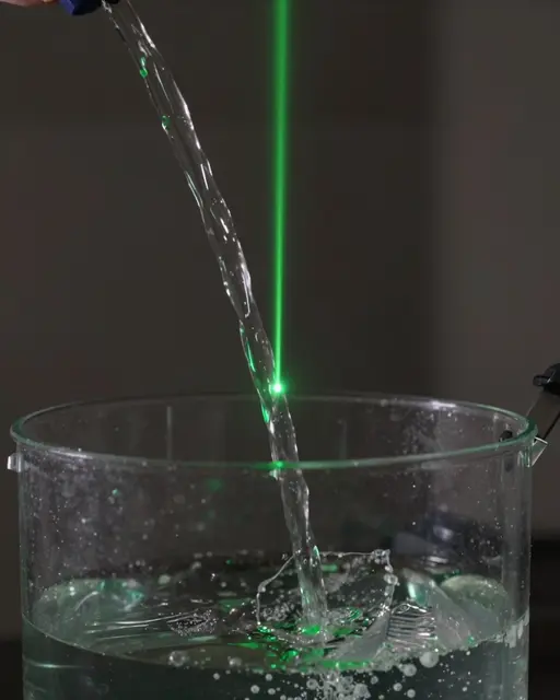 A green laser passes through a pouring water stream into a clear container in a dark room