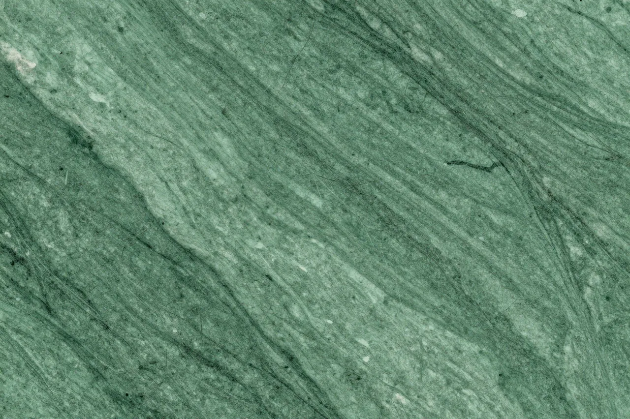 A close-up view of polished green marble with natural flowing veining across its surface