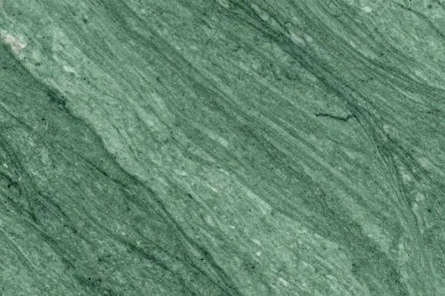 A close-up view of polished green marble with natural flowing veining across its surface