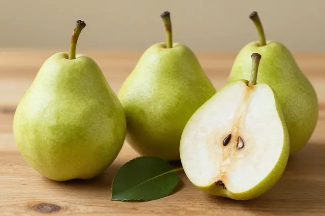 Three whole green pears and one halved pear sit with a leaf on a light wooden table
