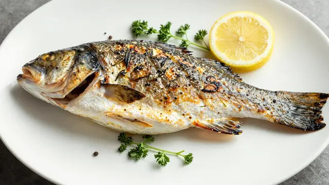 Whole grilled sea bass served on a white plate with a lemon slice and fresh parsley