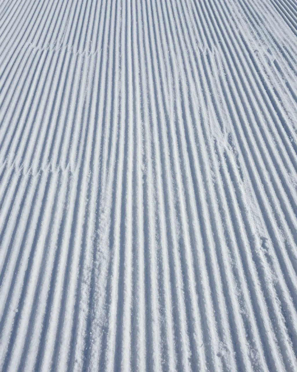 Top view of fresh parallel ridged groomed snow filling the entire frame, lit by side light