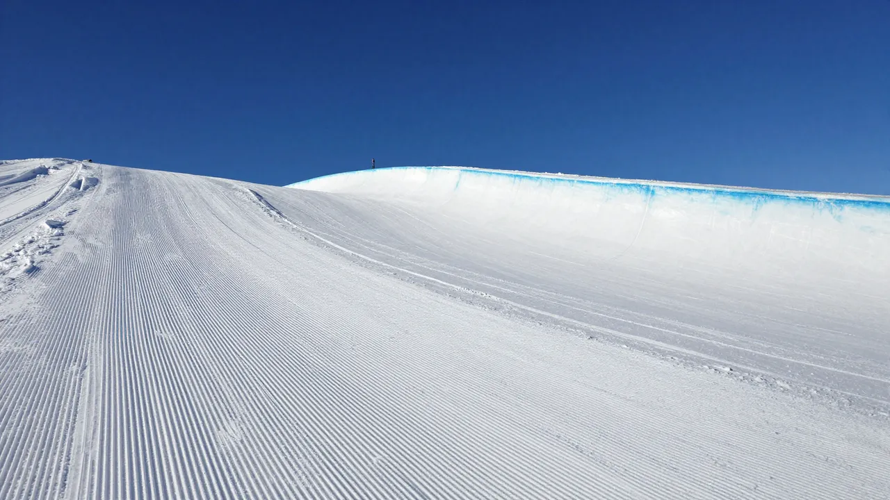 Freshly groomed empty snow halfpipe sits under a clear deep blue sky