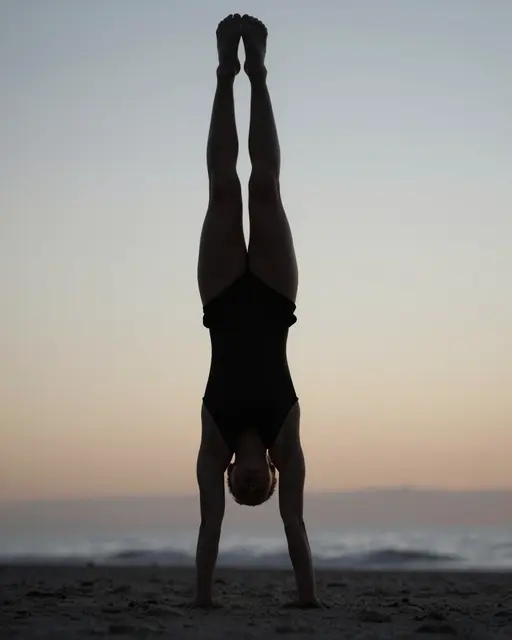 Silhouette of a gymnast holding a handstand on a sandy beach during soft dawn twilight