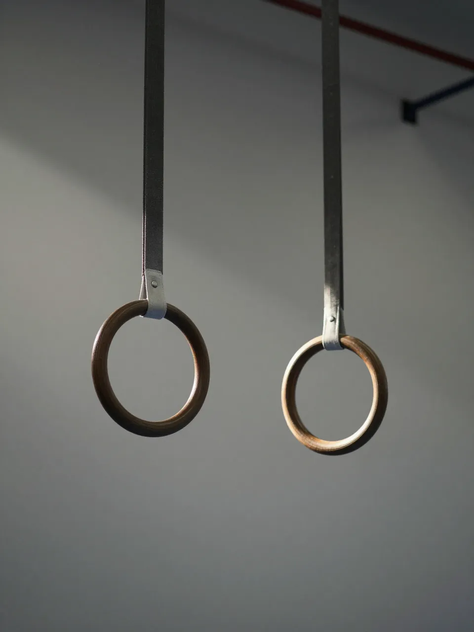 Wooden gymnastics rings hang from straps in an empty gym lit by soft morning light