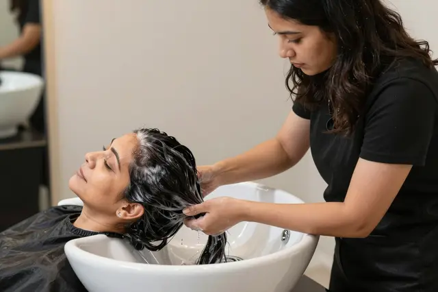 A salon stylist washes a client's hair over a white hair washing basin