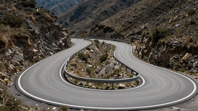 Winding paved mountain pass road with hairpin turns cuts through rocky arid high elevation hills