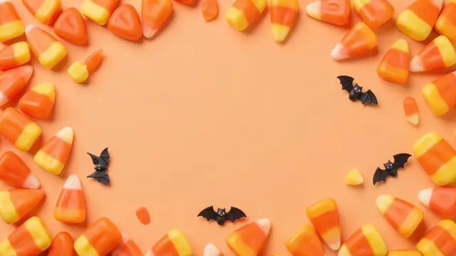 A top-down flat lay of candy corn and small decorative bats framing blank pastel orange copy space.