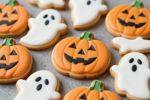 Iced jack-o'-lantern and ghost shaped Halloween sugar cookies arranged on a matte gray surface