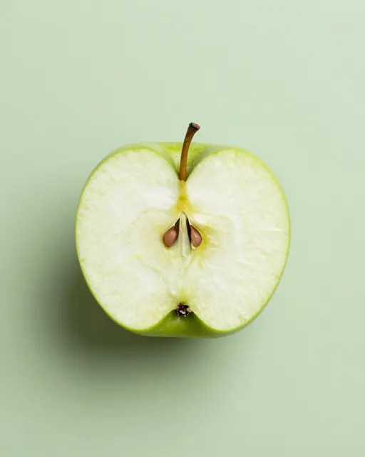 A top-down view of a halved green apple resting on a pale green solid background