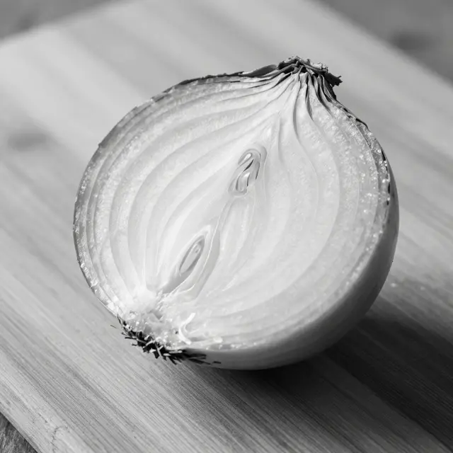 Black and white close-up of a cut onion showing concentric rings resting on a wooden cutting board