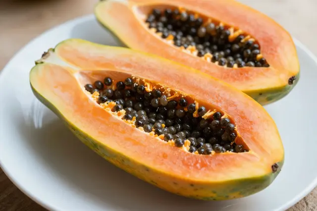 Two ripe papaya halves with black seeds rest on a white ceramic plate.