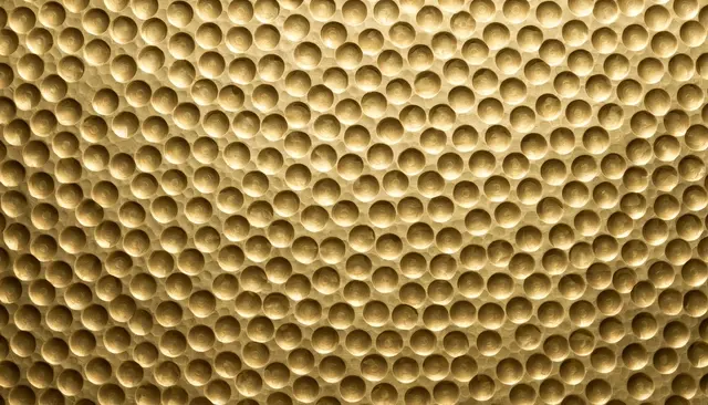 Full frame close-up of smooth golden hammered brass covered in uniform round dimples under even soft lighting