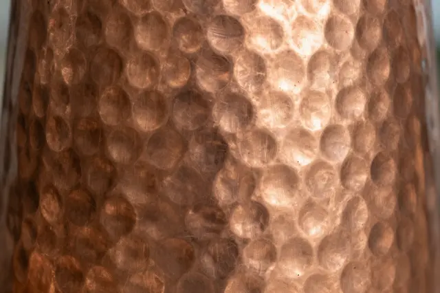 Close-up of warm dimpled hammered copper metal with soft glowing reflections across its patterned surface