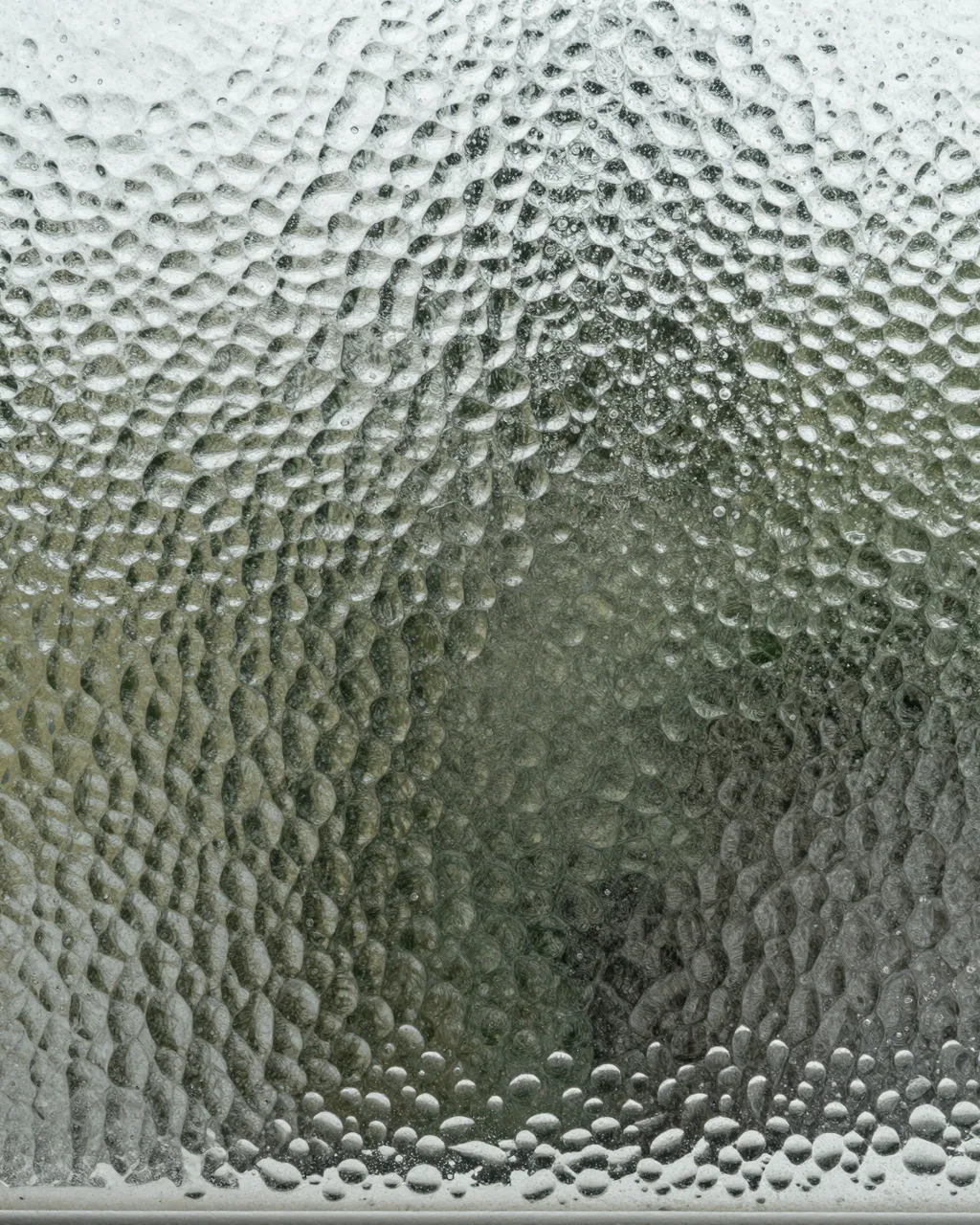 Full frame close-up of dimpled hammered glass scattering soft cool daylight.
