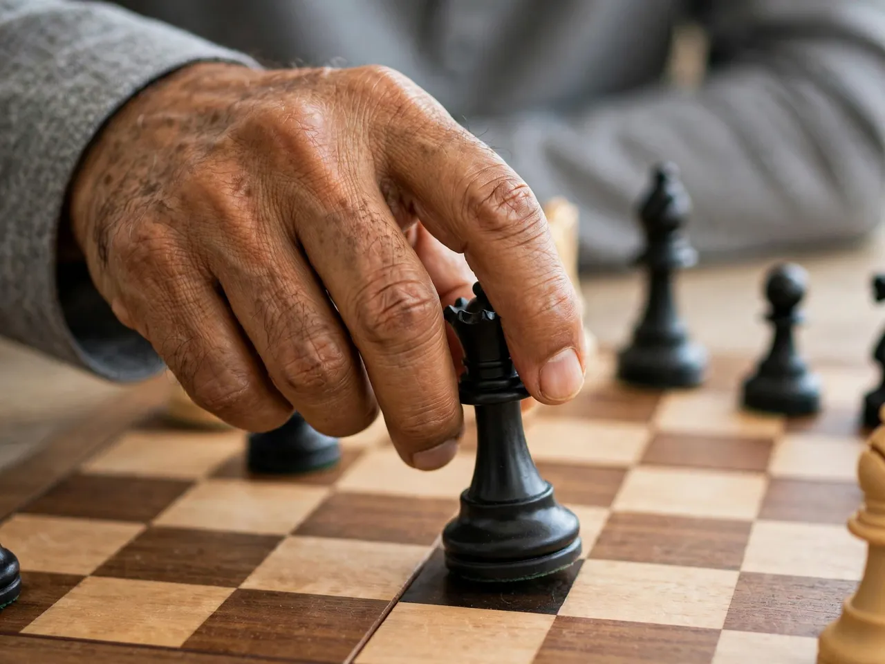 Close-up of a senior man's hand moving a black chess queen across a wooden chessboard