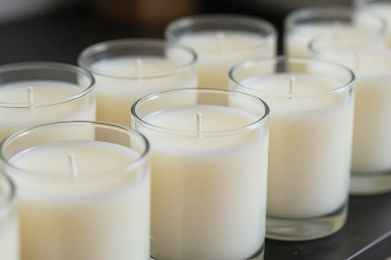 Row of plain glass jar candles with wicks set cooling on a dark work surface