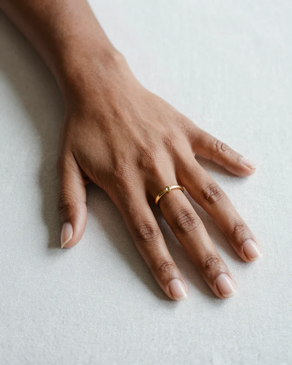 Close-up of a Black woman's hand resting on a light linen surface, wearing a simple gold band ring