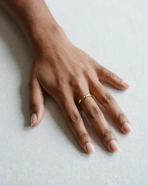 Close-up of a Black woman's hand resting on a light linen surface, wearing a simple gold band ring