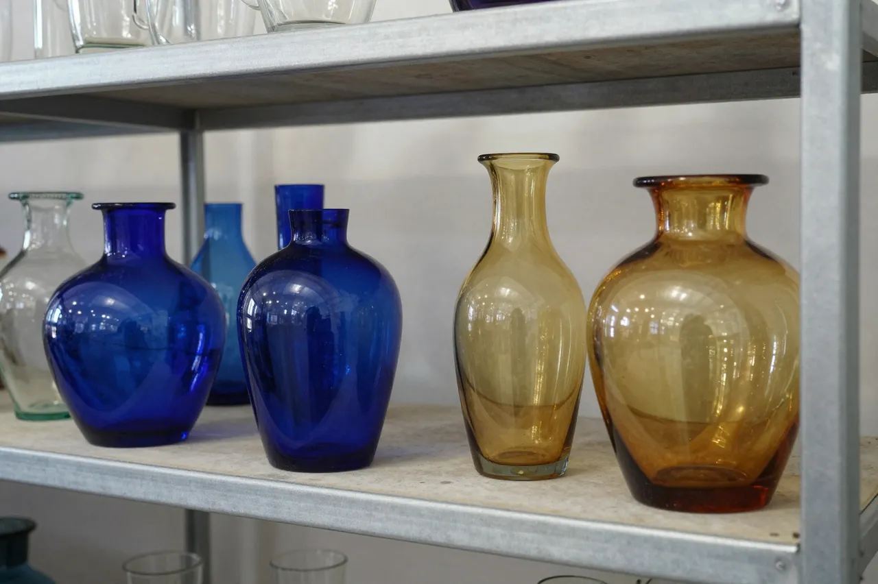 Cobalt blue, amber and clear handblown glass vases rest on a metal studio storage shelf.