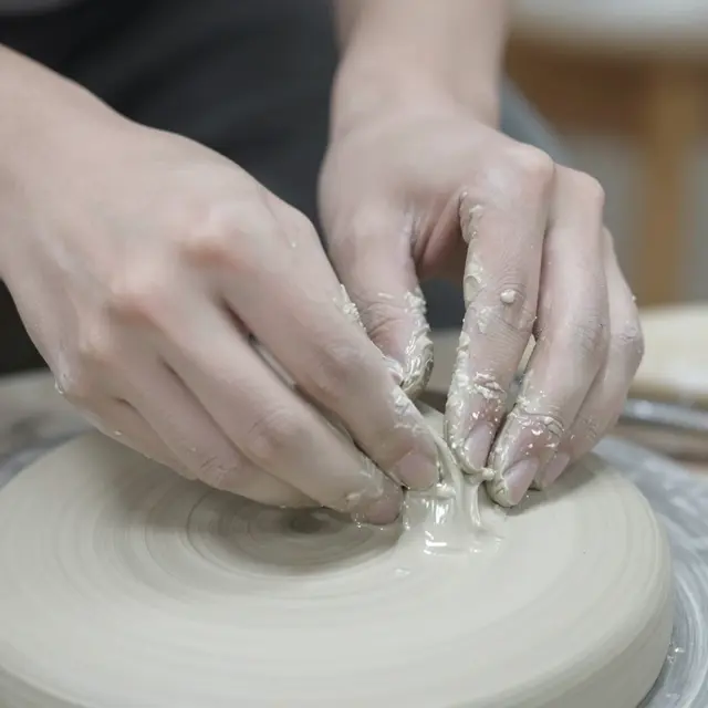 Close-up of ceramic artist's clay-covered hands smoothing wet clay on a spinning pottery wheel
