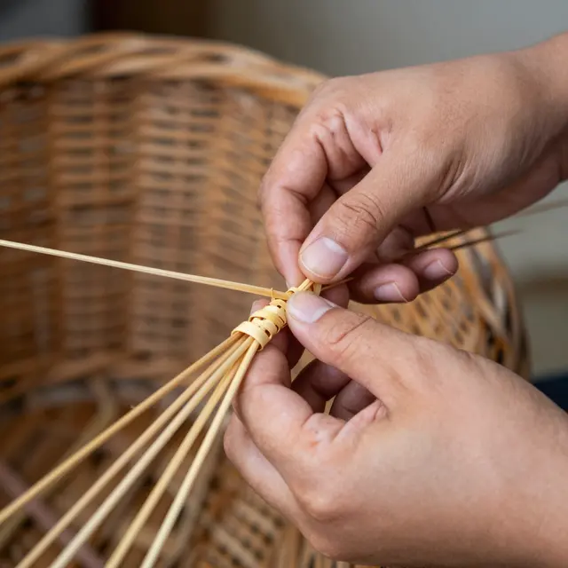 Close-up of a craftsperson's hands weaving thin willow strips to form a basket base