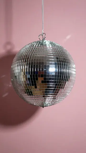 A mirrored disco ball hangs from string against a solid soft pink wall